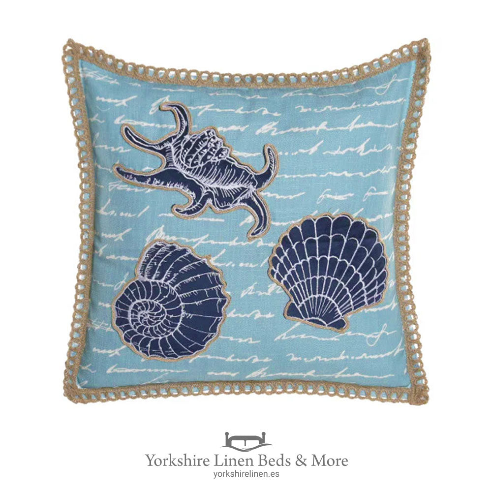 Embroidered coastal cushion featuring three large sea shells in gradient blue tones centered on a natural linen-style background – 45x45cm – Yorkshire Linen Mijas Costa.
